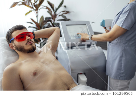 Young man receiving photo epilation while visiting beauty center on salon 101299565