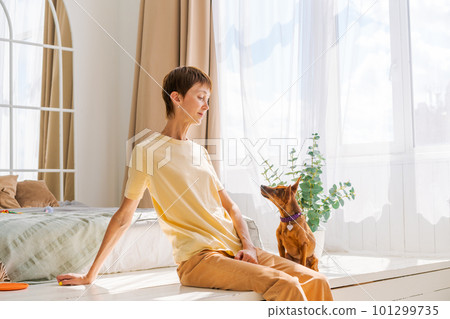 Owner playing with joyful dog at home, happy mature woman enjoying exercise 101299735