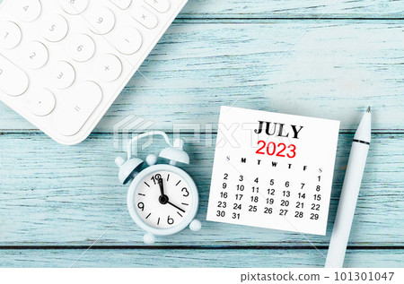 The July 2023 Monthly calendar year and alarm clock with calculator on blue wooden background. 101301047