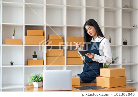 Startup SME small business entrepreneur of freelance Asian woman using tablet and box to receive and review orders online to prepare to pack sell to customers, online sme business ideas 101302046