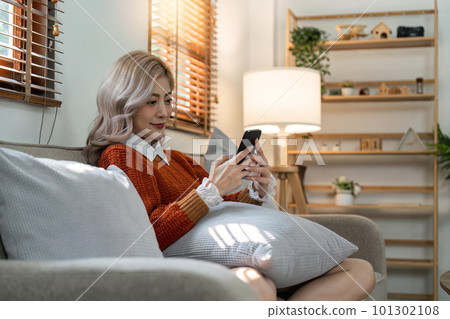 Happy young asian woman on mobile phone while sitting a couch in living room at home, Shopping online via website Happy young asian woman on mobile phone while sitting a couch in living room at home, Shopping online via website 101302108