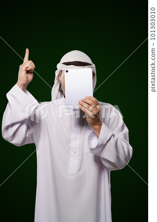 Muslim anonymous concept. Arab person holds digital tablet, face covered, index finger up, representing the concept of Islamic censorship online. Image portrays issues of privacy, security, and 101303010