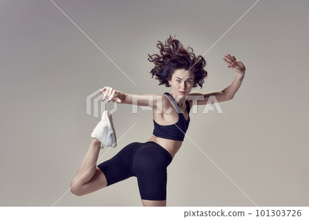Dynamic postural training. Young beautiful woman in sportswear training, posing in motion against grey studio background Dynamic postural training. Young beautiful woman in sportswear training, posing in motion against grey studio background 101303726