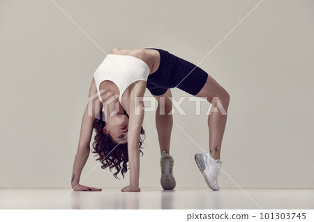Standing on bridge exercises. Flexible young woman in sportswear training, doing stretching exercises against grey studio background 101303745
