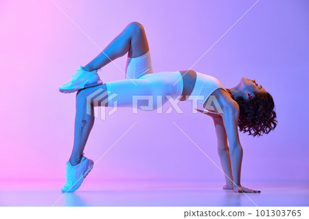 Young athletic woman with perfect fit body in white sportswear training against gradient pink blue background in neon light. Strength Young athletic woman with perfect fit body in white sportswear training against gradient pink blue background in neon light. Strength 101303765