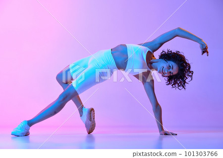 Flexibility of movements. Young woman with perfect fit body in white sportswear training against gradient pink blue background in neon light 101303766