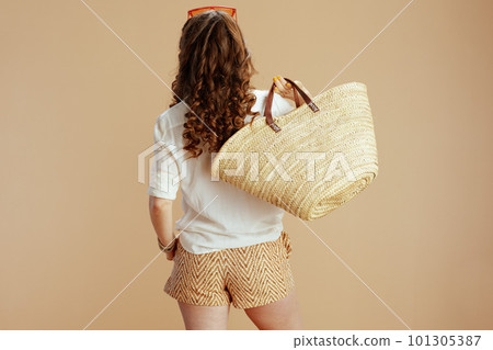 Seen from behind woman in blouse and shorts against beige 101305387