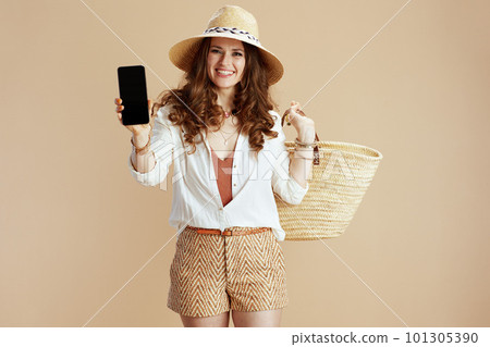 smiling stylish woman showing smartphone blank screen on beige smiling stylish woman showing smartphone blank screen on beige 101305390