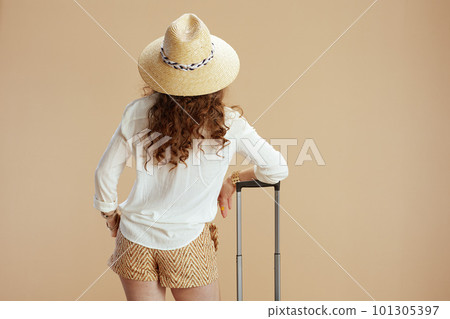 Seen from behind woman in blouse and shorts on beige 101305397