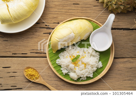 Cooked sweet glutinous rice topped with yellow bean and durian fruit,served with sweet coconut milk on wooden plate.Top view Cooked sweet glutinous rice topped with yellow bean and durian fruit,served with sweet coconut milk on wooden plate.Top view 101305464