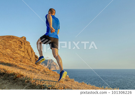 back male runner run uphill mountain trail in blue sky background, summer jogging along coast at sunset 101306226