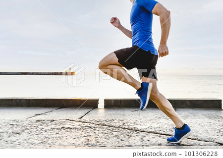 male runner running embankment in sunrise, summer jogging along seashore in background rising sun and lighthouse 101306228