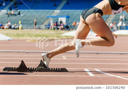 close-up female sprinter start from starting blocks run on stadium track, summer athletics competition 101306240