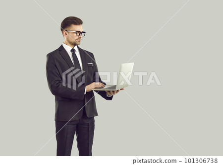 Serious businessman standing isolated on gray background and working on laptop computer 101306738