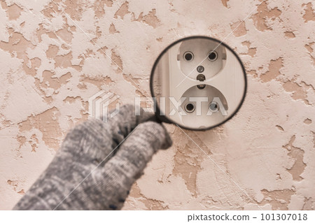 The hand of a construction worker in protective gloves examines through a magnifying glass the connection of appliances in the house The hand of a construction worker in protective gloves examines through a magnifying glass the connection of appliances in the house 101307018