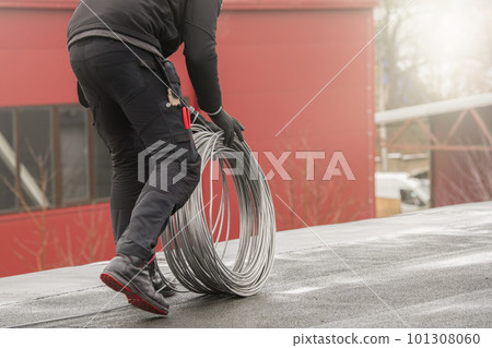 Ground wire. A worker lays a ground cable on the roof of a building. Electrician fixing aluminum wire for grounding solar panels 101308060