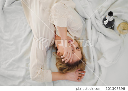 top view. blonde in delicate pajamas in bed with a champagne top view. blonde in delicate pajamas in bed with a champagne 101308896