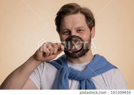 Caucasian man holding magnifier glass on teeth, looking at camera showing funny smiling face mouth Caucasian man holding magnifier glass on teeth, looking at camera showing funny smiling face mouth 101309650