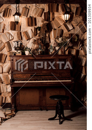 An old piano in a dark room. Lots of books on the walls 101309934