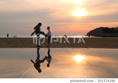 夕陽西下，一對父子在沙灘上模仿踢腿 101314290