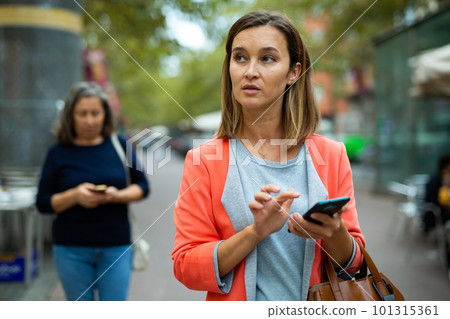 Interested female tourist using phone while walking through city 101315361