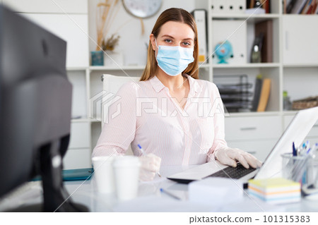 Businesswoman in protective medical mask is working with project behind laptop 101315383