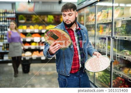 Young man shopping at supermarket food department, choosing frozen pizzas 101315400