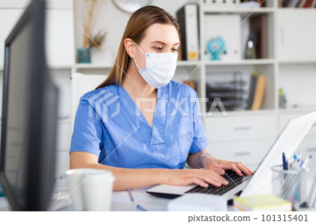 Woman doctor in face mask working on laptop 101315401