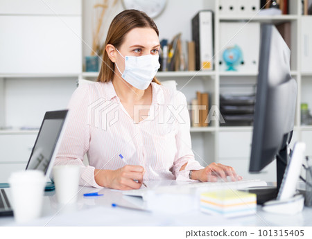 Woman in protective face mask working at office 101315405
