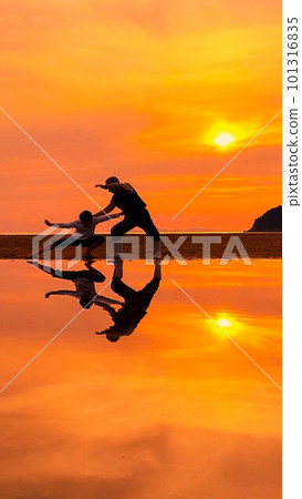 A silhouette of a woman and a boy imitating martial arts on the beach with the setting sun in the background 101316835