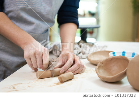 Woman cutting clay with blade standing behind table in studio 101317328
