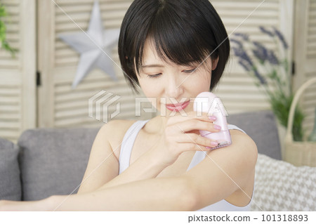 一位女士在客廳用家用脫毛器在手臂上進行自我脫毛 一位女士在客廳用家用脫毛器在手臂上進行自我脫毛 101318893