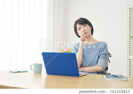 A woman in a wheelchair thinking while using a laptop in the living room A woman in a wheelchair thinking while using a laptop in the living room 101318911