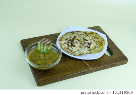 roti canai and curry sauce in white plate with served on the wooden chopping board. 101319569