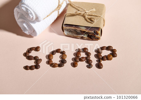 Top view of coffee beans laid out in SOAP word on pink background with natural soap bar - a body scrub and white towel. Anti-cellulite treatment. Home spa. Body and skin care concept. Still life 101320066