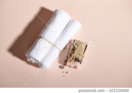 Flat lay white towels near cold pressed handmade natural organic soap bar, wrapped in craft eco paper and scattered lavender flowers on isolated pink background. Spa and beauty care concept Still life 101320080