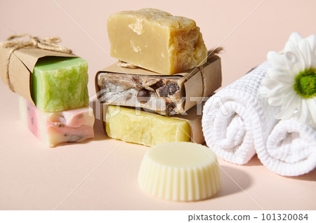 Still life with assortment of handmade soap bars and dry shampoos with organic natural ingredients and chamomile flower on a white terry towel, isolated on pink. Hygiene and purity, body care concept 101320084