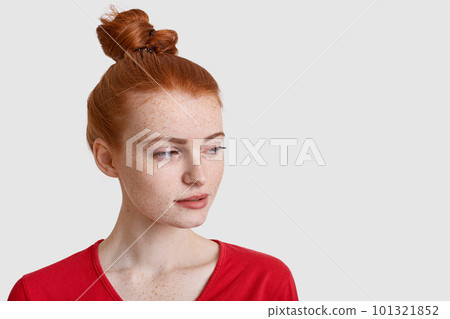 Headshot of beautiful redhead woman focused aside with thoughtful expression, has hair knot, freckled face, being deep in thoughts, isolated over white background with copy space for your text 101321852