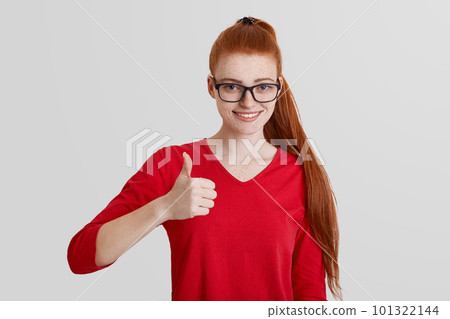 Portrait of cheerful redhaired female with freckled skin, shows like, raises thumb, approves somebody`s actions, dressed in red clothhes, isolated over white background. Optimistic woman indoor Portrait of cheerful redhaired female with freckled skin, shows like, raises thumb, approves somebody`s actions, dressed in red clothhes, isolated over white background. Optimistic woman indoor 101322144