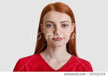 Headshot of attractive red haired European woman with freckled skin, looks seriously at camera, has minimal make up, wears red sweater, isolated over white background. Natural beauty concept Headshot of attractive red haired European woman with freckled skin, looks seriously at camera, has minimal make up, wears red sweater, isolated over white background. Natural beauty concept 101322154