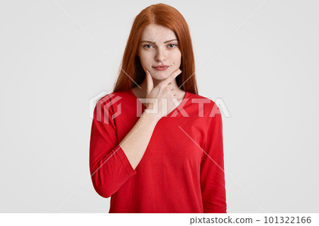 Waist up portrait of serious foxy female holds chin, has freckles skin, dressed in red casual sweater, being self confident, isolated over white background. People, beauty and lifestyle concept Waist up portrait of serious foxy female holds chin, has freckles skin, dressed in red casual sweater, being self confident, isolated over white background. People, beauty and lifestyle concept 101322166