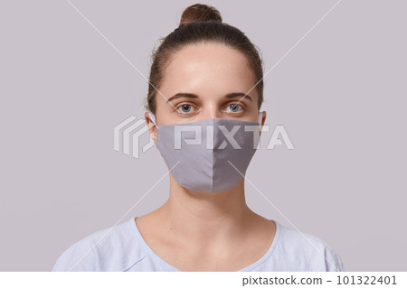 Closeup portrait of serious woman wearing gray protective mask, lady dresses white casual t shirt looking directly at camera, posing isolated over white background. Corona virus protection concept. Closeup portrait of serious woman wearing gray protective mask, lady dresses white casual t shirt looking directly at camera, posing isolated over white background. Corona virus protection concept. 101322401