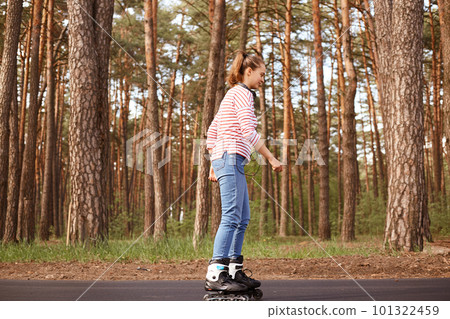 Outdoor shot of attractive woman dresses casual attire rollerblading in forest during her weekend. Lady spending time in open air, enjoying nature, being in good mood. People lifestyle concept. Outdoor shot of attractive woman dresses casual attire rollerblading in forest during her weekend. Lady spending time in open air, enjoying nature, being in good mood. People lifestyle concept. 101322459