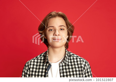 Close up portrait of young boy wearing checkered shirt looking at camera with fake smile over red studio background Close up portrait of young boy wearing checkered shirt looking at camera with fake smile over red studio background 101322807