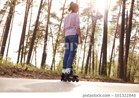 Back view of female dresses casual attire rollerblading outdoors, spending her free time in forest, breathing fresh air, looking in distance, enjoying beautiful nature. People lifestyle concept. 101322848