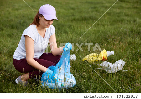 Woman picking up plastic bottles and rubbish from meadow, environmental activist collecting plastic garbage, volunteer picking up single used plastic in green field. 101322918