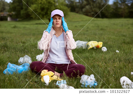 Tired environmental activist sitting on green grass with fingers on temples, exhausted female picking up trash in park, being in despair, calls for sorting litter and throw garbage in designated areas Tired environmental activist sitting on green grass with fingers on temples, exhausted female picking up trash in park, being in despair, calls for sorting litter and throw garbage in designated areas 101322927