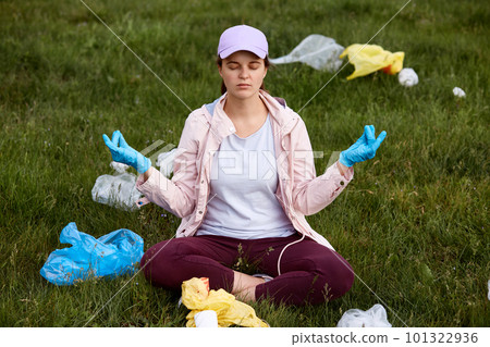 Young girl shocked by mud in field, trying to calm down, meditates, being very upset, surrounded with rubbish, keeping eyes closed, being sad of ecological problems. 101322936