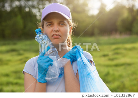 Portrait of young female volunteer posing outdoor, collecting garbage, woman in casual clothing picking up waste in field, land pollution, environmental problem. 101322967