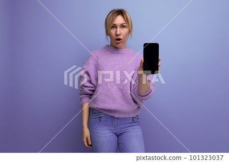 portrait of a surprised blond young woman in a lilac sweater with a smartphone mockup on a bright portrait of a surprised blond young woman in a lilac sweater with a smartphone mockup on a bright 101323037